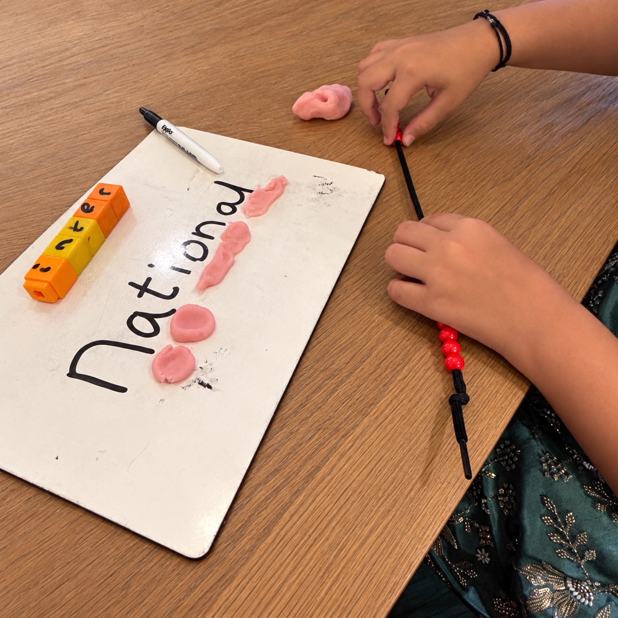 A child exploring spelling using letter cubes, playdough and beads
